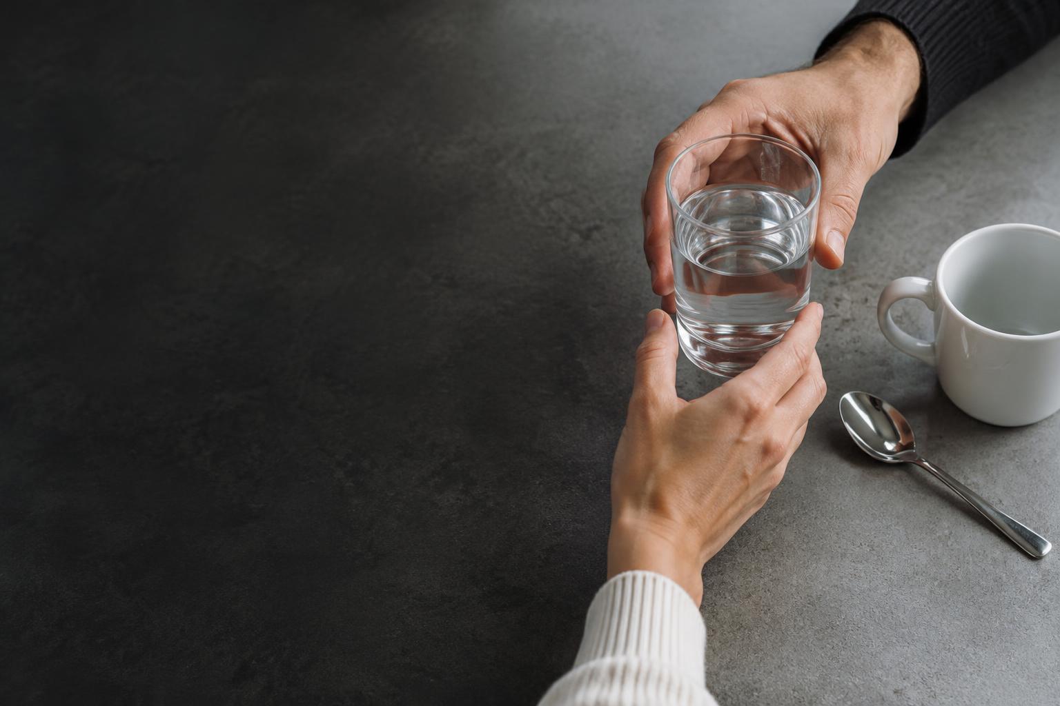 Hands passing a glass on a worktable — illustrative task imagery